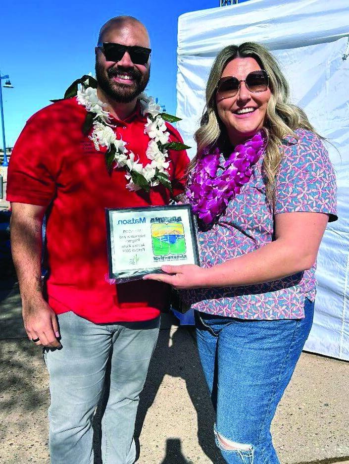 澳博体育app下载 employees wearing sunglasses and adorned with leis hold a frame with the festival's Mahalo award.